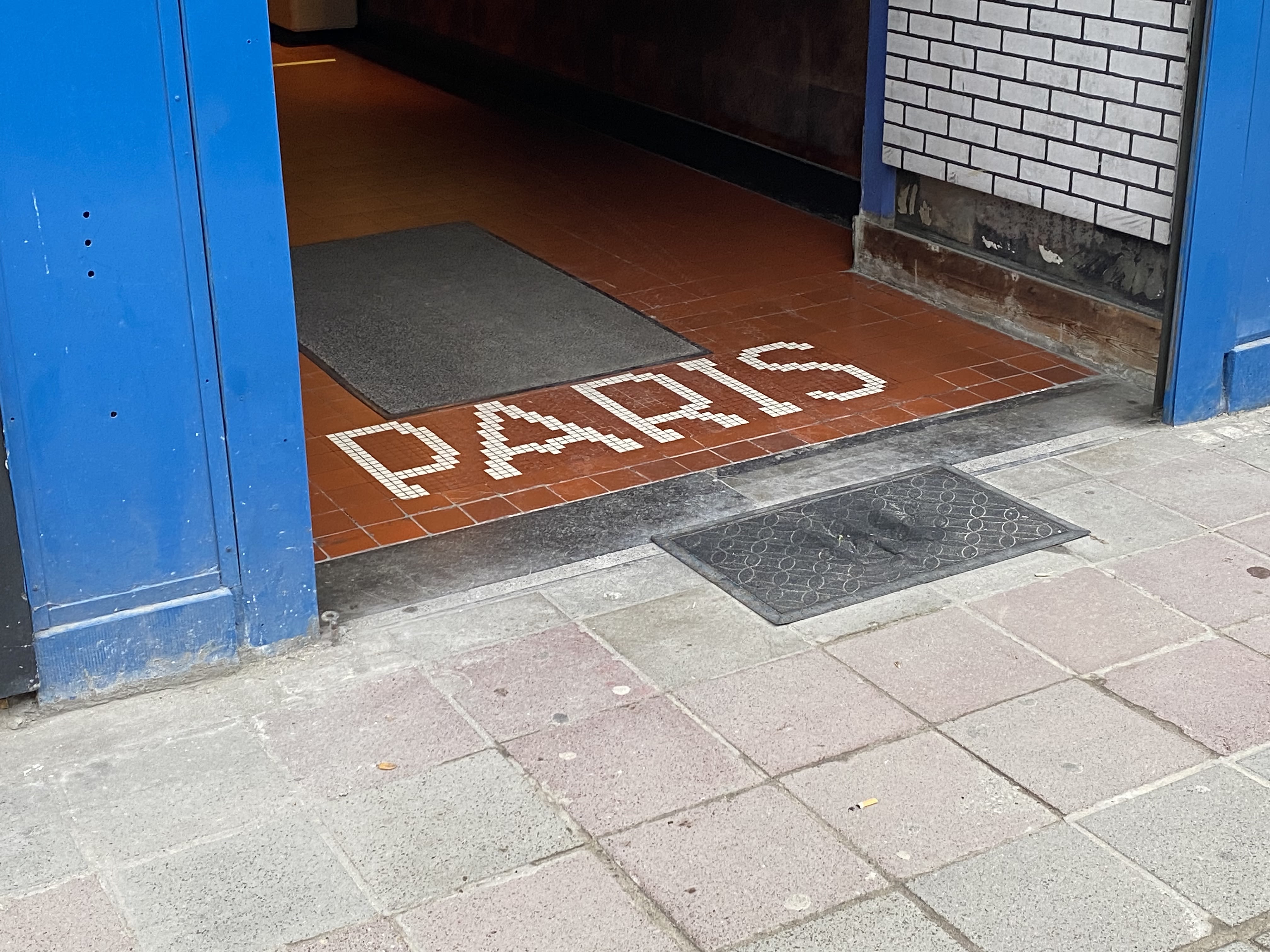 Entrée du cinéma paris. On aperçoit le seuil de l'entrée sur lequel il est écrit en toutes lettres "paris". On distingue aussi un paillasson